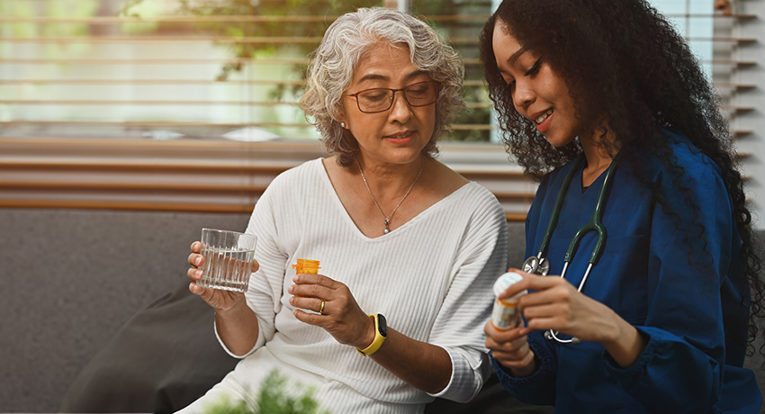 A young nurse or caregiver in scrubs showing a medicine bottle to an older female patient
